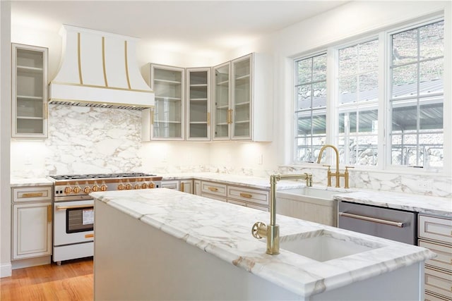 kitchen with decorative backsplash, custom range hood, light stone counters, stainless steel appliances, and light wood-type flooring