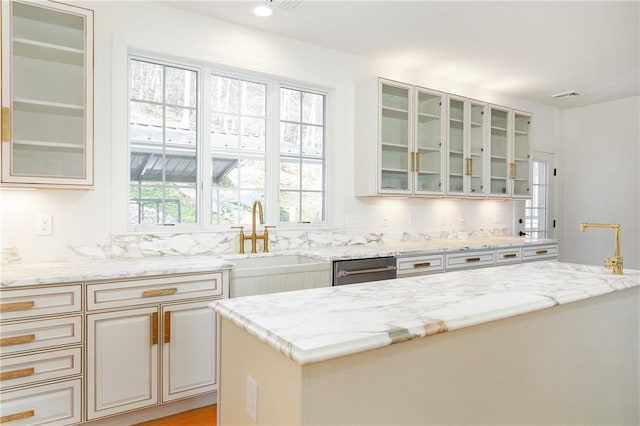 kitchen featuring recessed lighting, glass insert cabinets, a sink, light stone countertops, and dishwasher