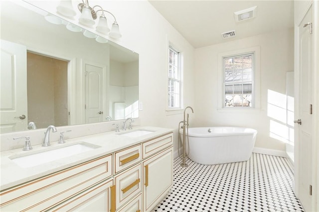 bathroom with double vanity, a freestanding tub, visible vents, and a sink