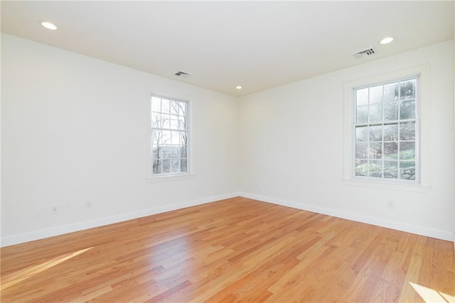 empty room featuring light wood-type flooring, visible vents, baseboards, and recessed lighting