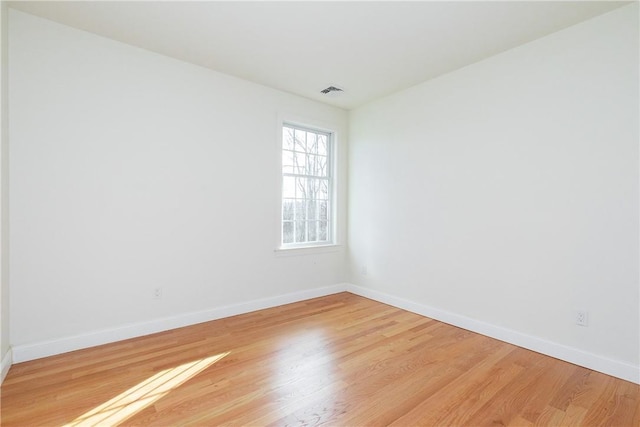 empty room with light wood finished floors, visible vents, and baseboards