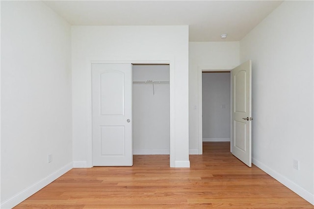 unfurnished bedroom with light wood finished floors, baseboards, and a closet