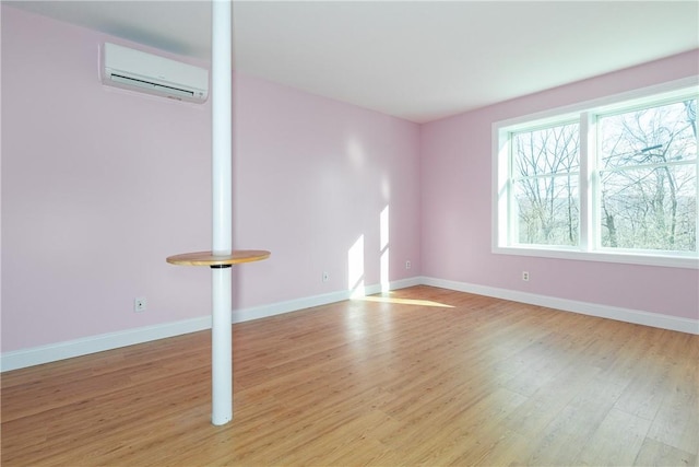 unfurnished room featuring a wall unit AC, light wood-style flooring, and baseboards