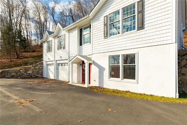 view of side of home with a garage, aphalt driveway, and stucco siding