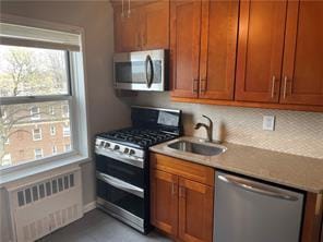 kitchen featuring stainless steel appliances, radiator, brown cabinets, and a sink