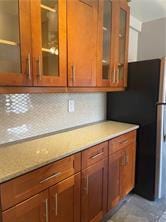 kitchen featuring freestanding refrigerator, glass insert cabinets, and brown cabinets