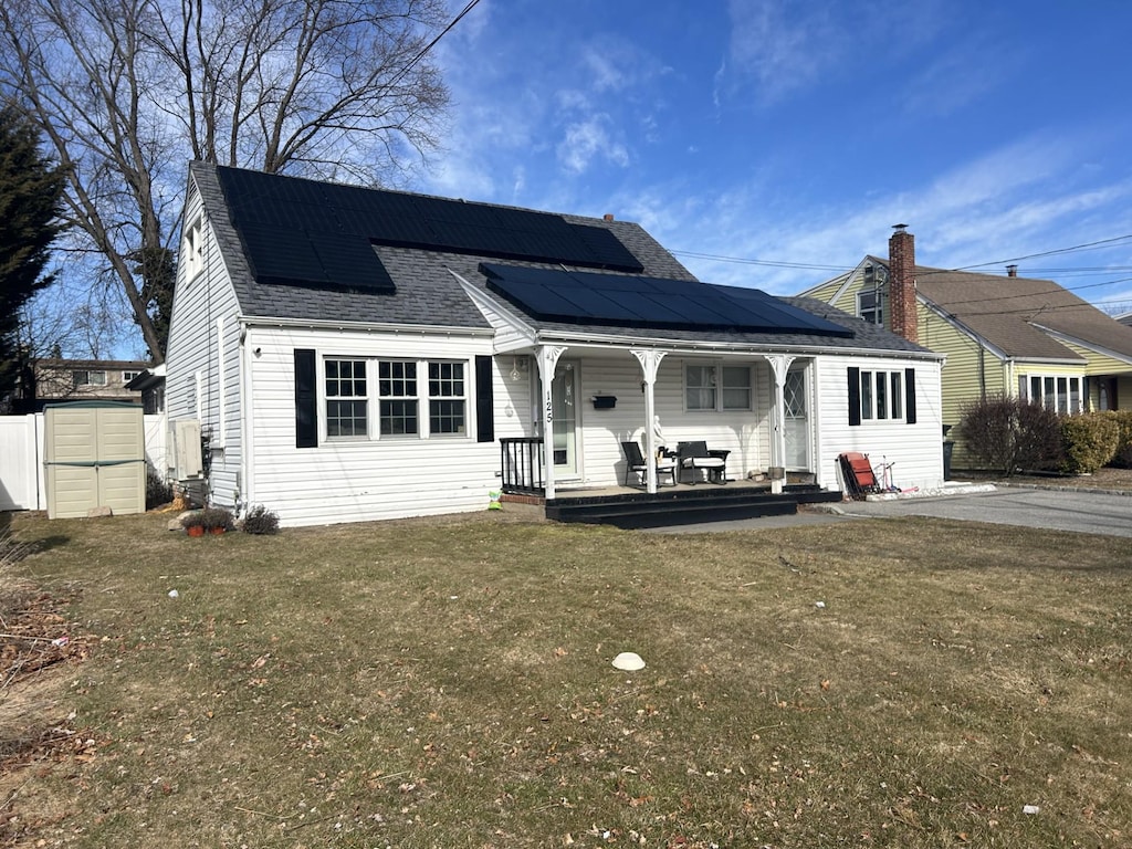 view of front of home with covered porch, solar panels, roof with shingles, and a front yard