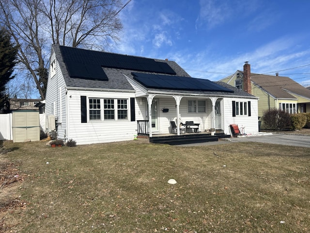 view of front of home with covered porch, solar panels, roof with shingles, and a front yard