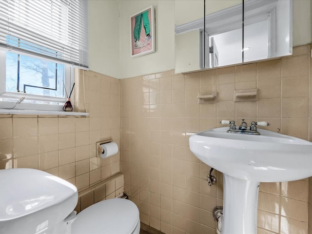 bathroom with a sink, toilet, and tile walls