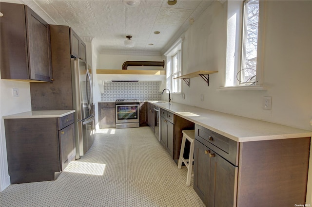 kitchen featuring open shelves, stainless steel appliances, light countertops, a sink, and dark brown cabinets
