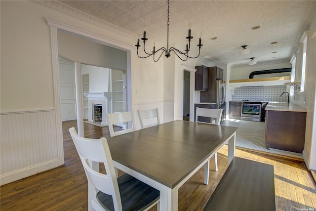 dining area featuring an ornate ceiling, a tile fireplace, a wainscoted wall, and wood finished floors