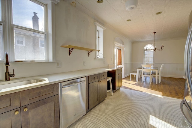 kitchen with crown molding, stainless steel appliances, light countertops, wainscoting, and a sink