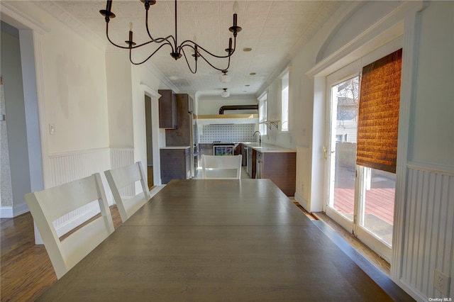 unfurnished dining area with a wainscoted wall, dark wood-type flooring, a sink, ornamental molding, and an inviting chandelier