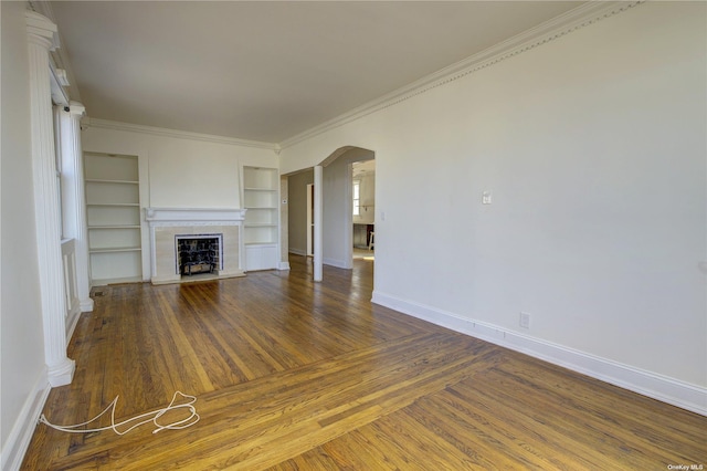 unfurnished living room with baseboards, arched walkways, wood finished floors, crown molding, and a fireplace