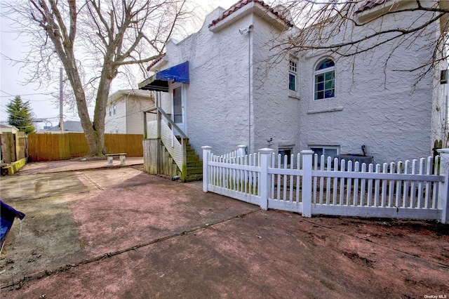 view of side of home featuring fence private yard, a tile roof, a patio area, and stucco siding