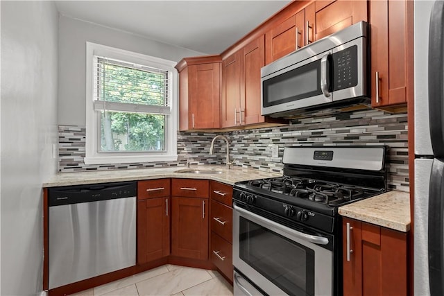 kitchen with light stone counters, a sink, tasteful backsplash, appliances with stainless steel finishes, and brown cabinetry