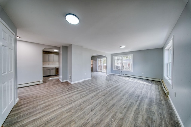 unfurnished living room featuring baseboards, arched walkways, light wood-style floors, a baseboard heating unit, and baseboard heating