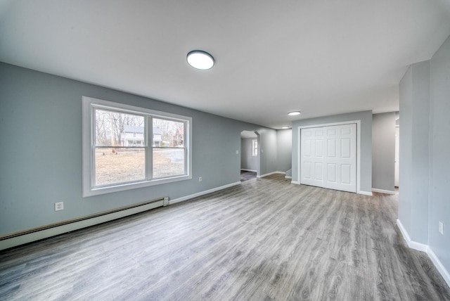 interior space featuring baseboards, stairs, baseboard heating, wood finished floors, and arched walkways