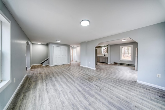 unfurnished living room with a baseboard radiator, arched walkways, baseboards, and wood finished floors