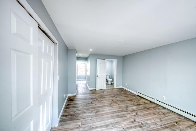 unfurnished room with a baseboard radiator, baseboards, and wood finished floors