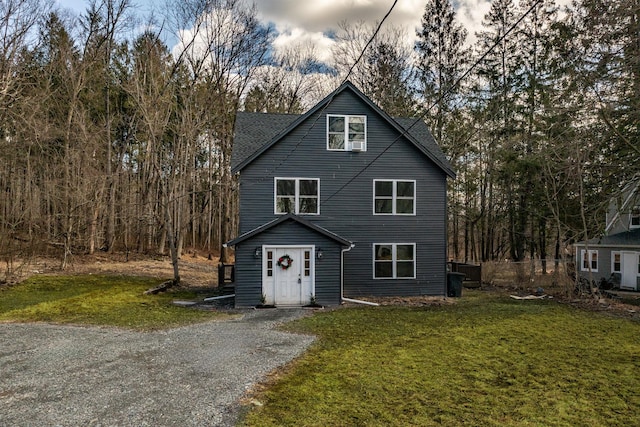 view of front facade featuring gravel driveway, a front lawn, and a shingled roof