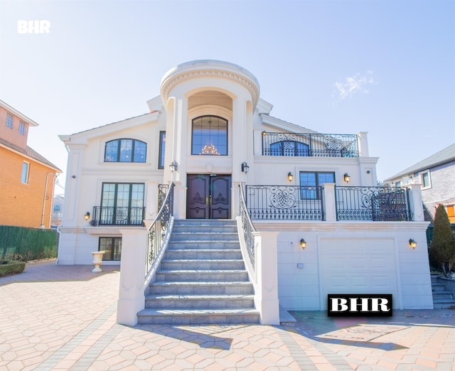 view of front of home with a balcony, a garage, french doors, and stucco siding