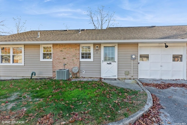 back of property featuring cooling unit, a yard, an attached garage, a shingled roof, and brick siding