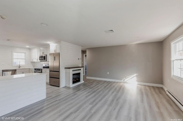 unfurnished living room featuring visible vents, light wood-type flooring, a sink, baseboards, and baseboard heating