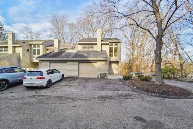 view of front of home with aphalt driveway, a chimney, a garage, and roof with shingles