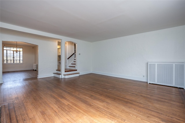 unfurnished living room with stairway, arched walkways, radiator, a chandelier, and dark wood-style flooring