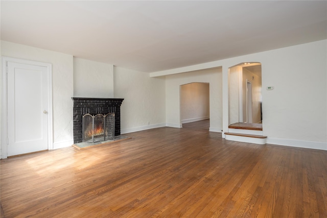 unfurnished living room with hardwood / wood-style floors, a fireplace, arched walkways, and baseboards