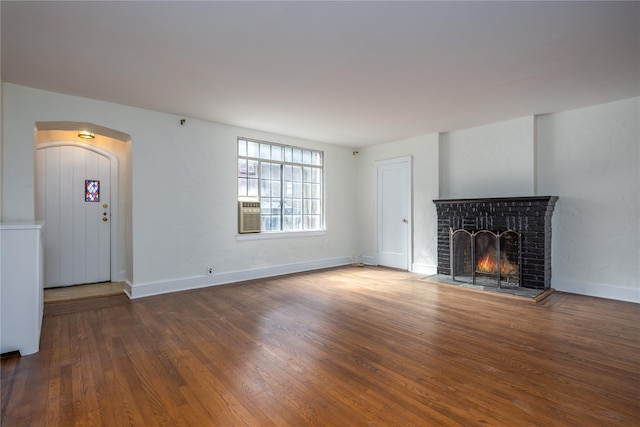 unfurnished living room with wood finished floors, a fireplace, baseboards, and arched walkways