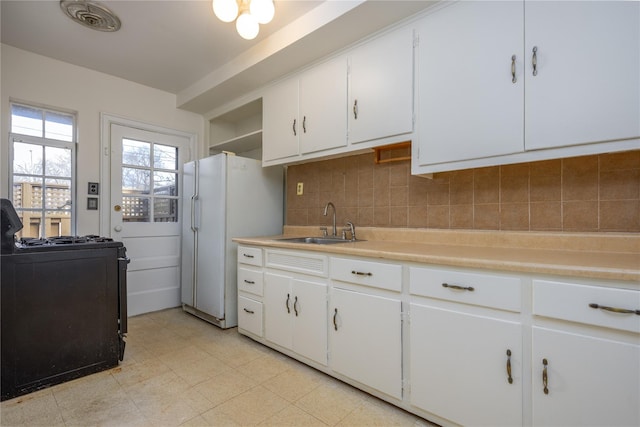 kitchen featuring a sink, backsplash, freestanding refrigerator, white cabinets, and gas range