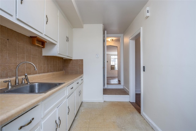 kitchen featuring decorative backsplash, light countertops, white cabinets, and a sink