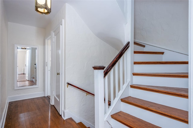 staircase featuring a textured wall, baseboards, and wood finished floors