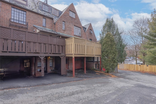 rear view of house featuring a wooden deck, a high end roof, brick siding, and fence