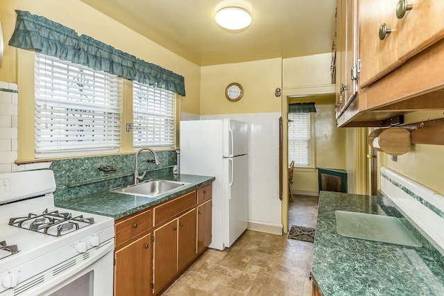 kitchen with a sink, white appliances, dark countertops, and brown cabinetry