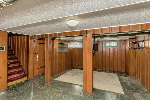 basement featuring stairway, wooden walls, and a healthy amount of sunlight