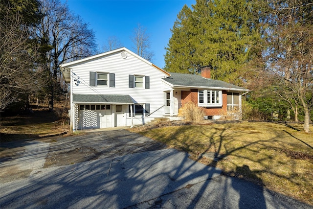 split level home featuring a front yard, a chimney, a garage, aphalt driveway, and brick siding