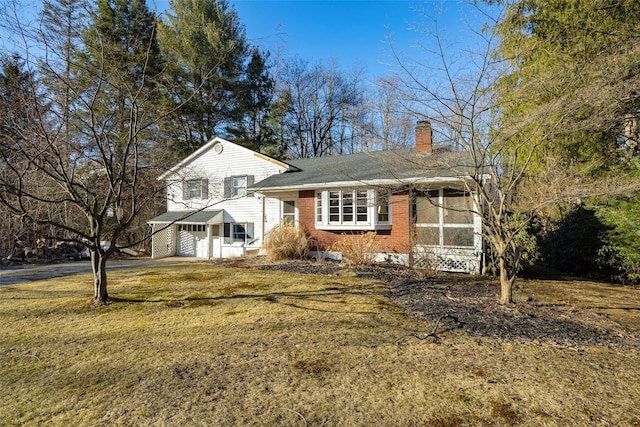 split level home featuring driveway, brick siding, a chimney, and a front lawn