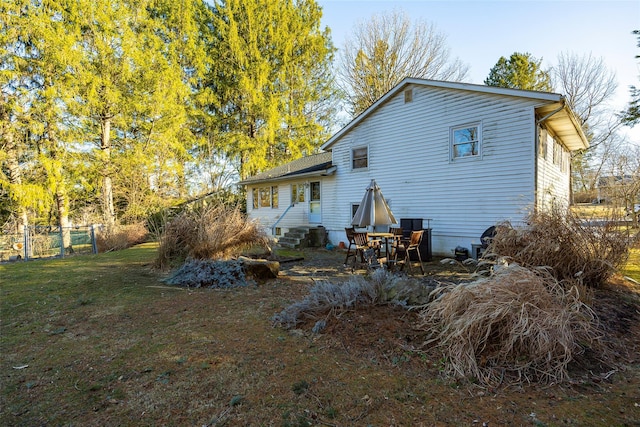 rear view of house with entry steps, a lawn, and fence