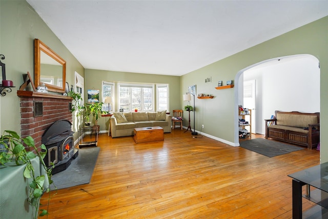 living room with arched walkways, light wood finished floors, a wood stove, and baseboards