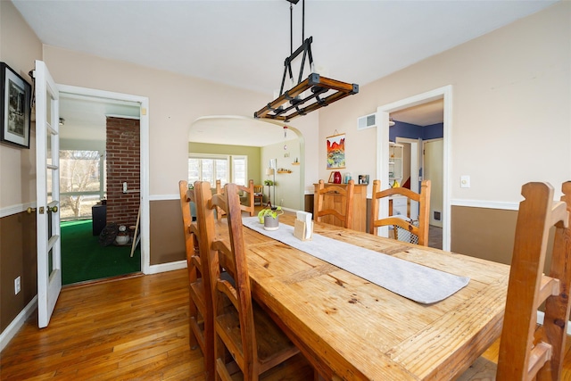 dining space with visible vents, arched walkways, baseboards, and hardwood / wood-style floors