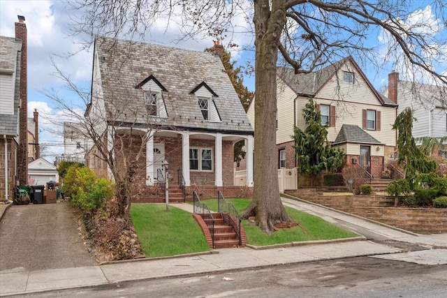 cape cod home featuring brick siding, a chimney, covered porch, a high end roof, and a front yard