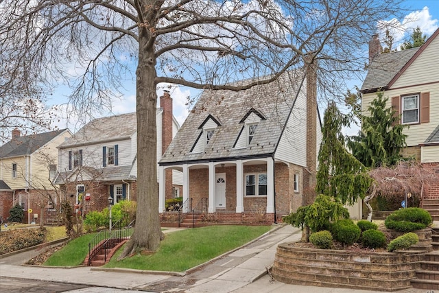 view of front facade with a porch, brick siding, a front lawn, a chimney, and a high end roof