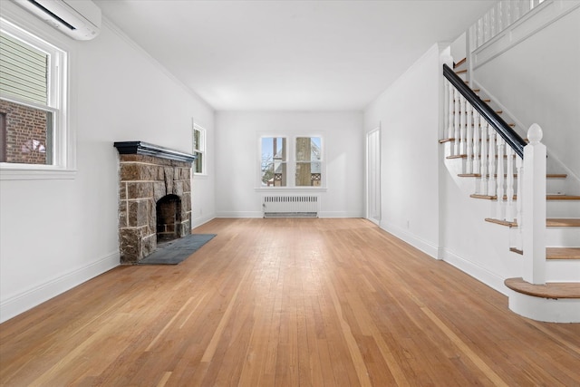 unfurnished living room featuring light wood finished floors, radiator, a stone fireplace, a wall mounted air conditioner, and stairs