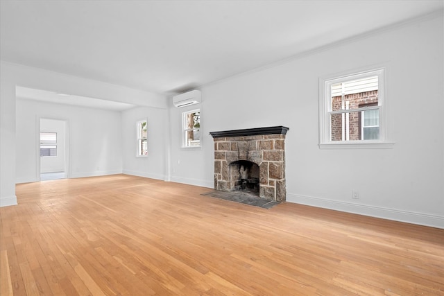 unfurnished living room featuring baseboards, a fireplace, a wall unit AC, and light wood-style floors