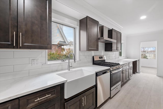 kitchen with a sink, dark brown cabinets, ornamental molding, appliances with stainless steel finishes, and wall chimney exhaust hood