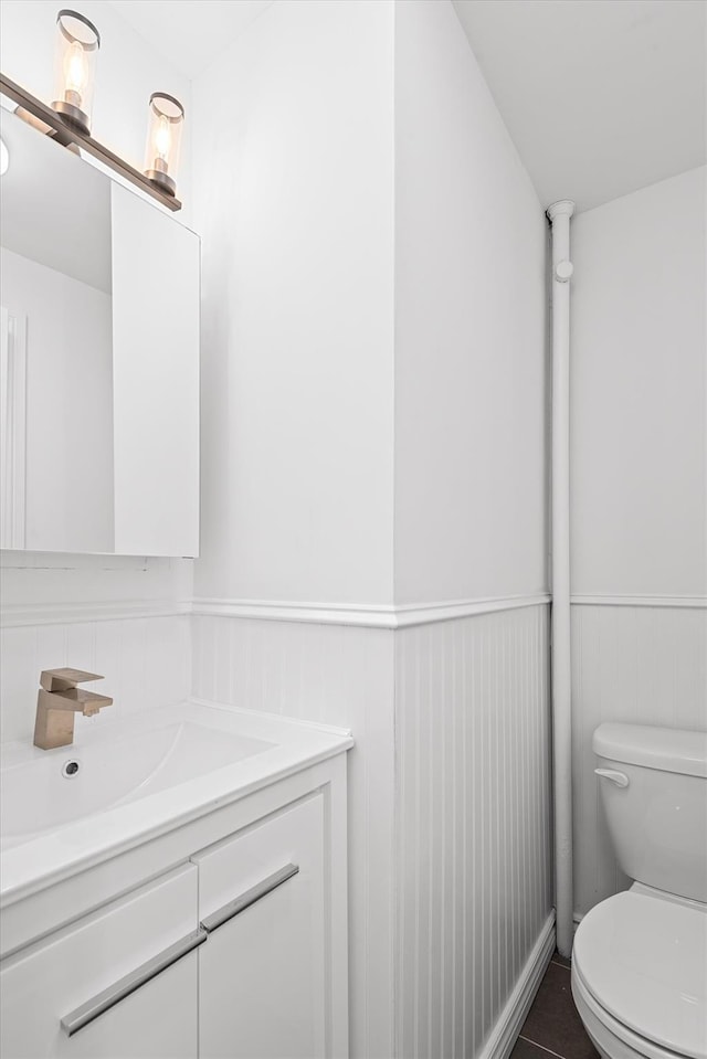 half bathroom featuring a wainscoted wall, vanity, and toilet