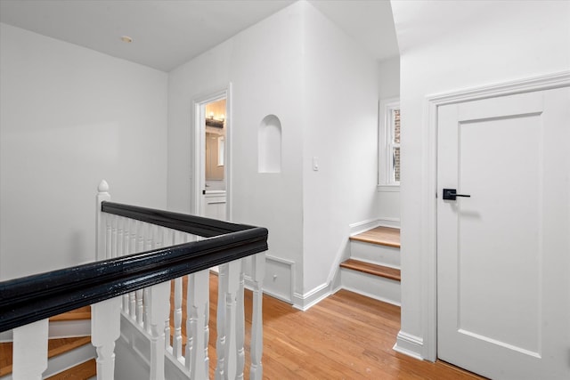 hall featuring baseboards, light wood-style flooring, and an upstairs landing